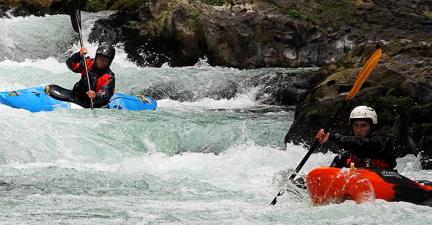 A man and a woman kayak through a rapid on an intermediate kayak instruction course.