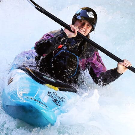 A female kayaker smiles at the camera while running a rapid on an intermediate kayak instrction course.