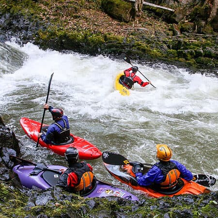 A group of kayakers watches a kayak practice ferrying on an intermediate kayak instruction course.