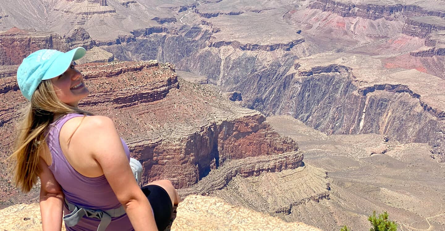 Kali Bennett sits in front of a large desert canyon - Wet Planet Whitewater office and reservations staff member.
