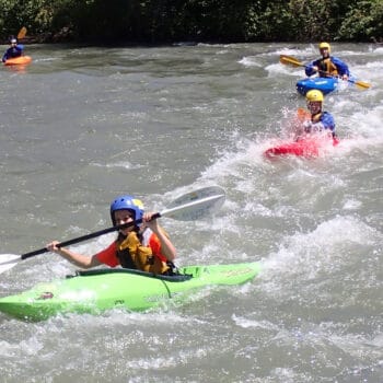 A group of kayakers on a youth kayaking program paddle in line through a class II rapid.