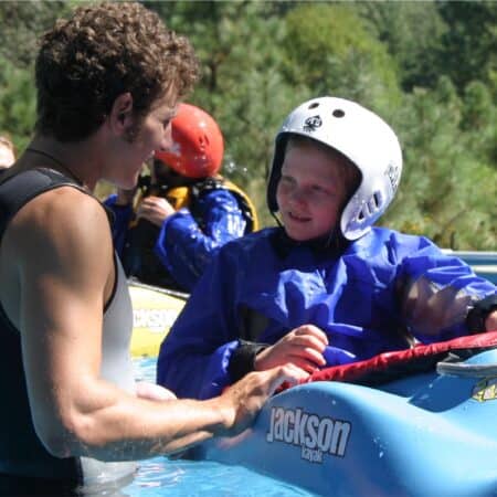 An instructor on the kids' kayaking camp holds onto the kayak of a young girl while explaining kayak technique.