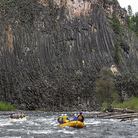Rafts paddle toward gigantic balsalt cliff walls on a Klickitat River rafting trip.