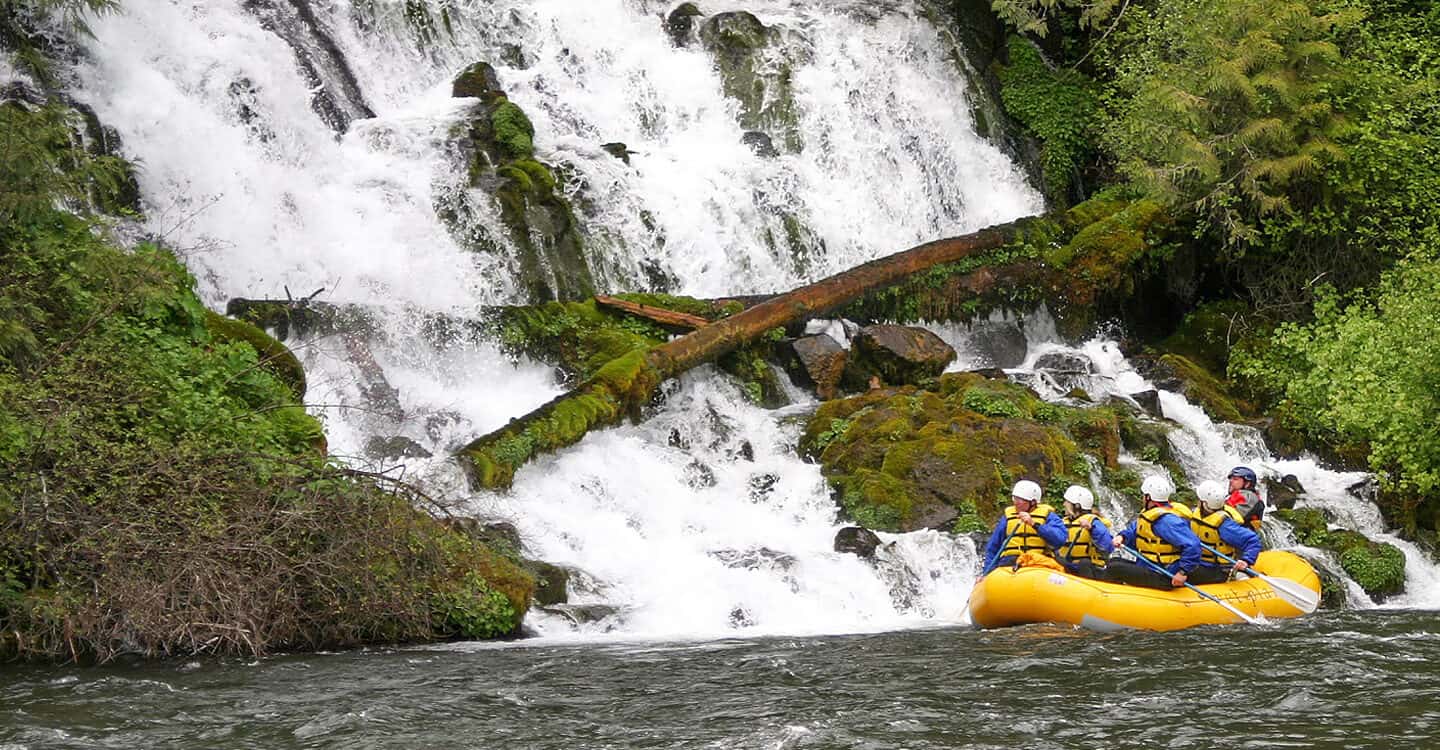 A group of rafters paddles past a waterfall on a Klickitat River Rafting trip in Washington.