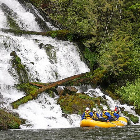 A group of rafters paddles past a waterfall on a Klickitat River Rafting trip in Washington.