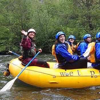 A raft guide waves and a rafter smiles at the camera on a Klickitat River rafting trip in Washington wet planet whitewater oregon