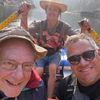 Two passengers in a raft take a selfie with the raft guide rowing behind them on the Main Salmon River in Idaho.