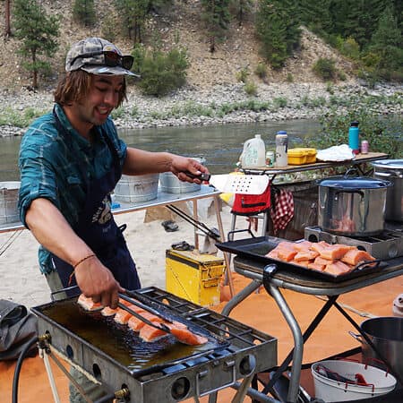 A student on an Idaho Main Salmon River rowing school cooks salmon on the grill in a group kitchen at camp.