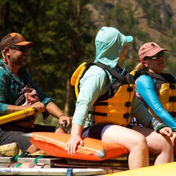 A close up image of a raft guide rowing two guests in the sun on Idaho's Main Salmon River.