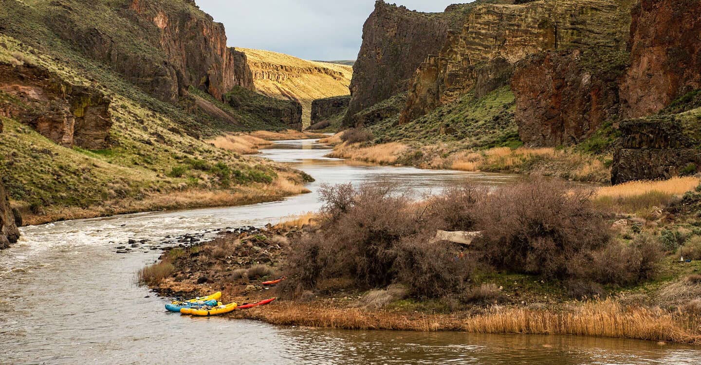 A scenic view showing rafts on the beach at camp with the Owyhee River canyon in the background.