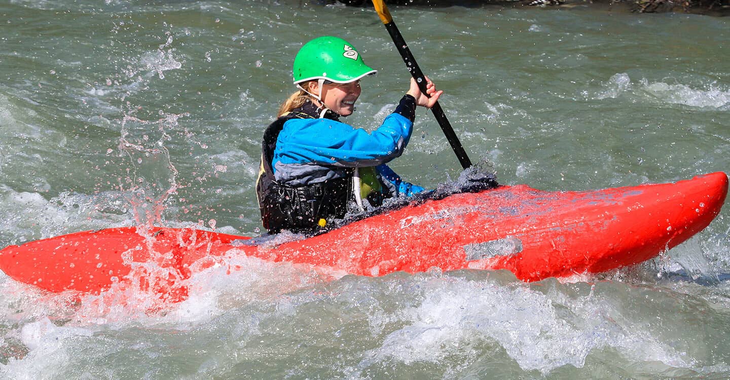 A female kayaking student paddles a rapid on a beginner kayaking course.