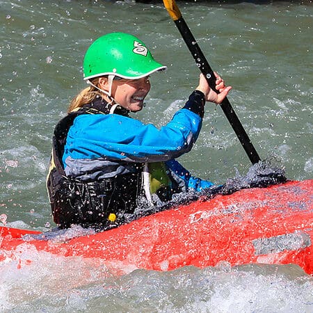 A female kayaking student paddles a rapid on a beginner kayaking course.