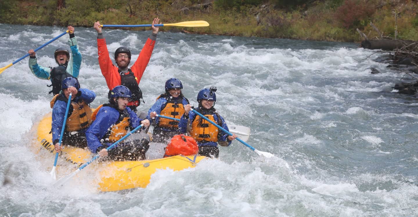 Rafters navigate rapids as guides hold up their paddles. Wet Planet Whitewater in Washington, Idaho, Oregon