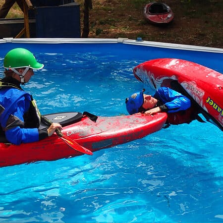 A female kayak instructor watches while a student practices a t-rescue during a kayak course pool session.