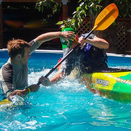 An instructor helps a student with their kayak roll during a pool session.