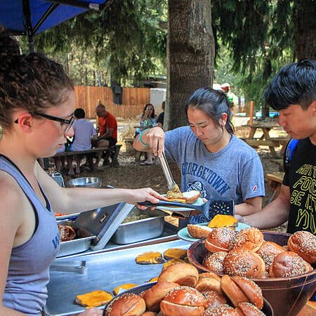 A Wet Planet employee serves a cheeseburger to a rafting guest at a BBQ.