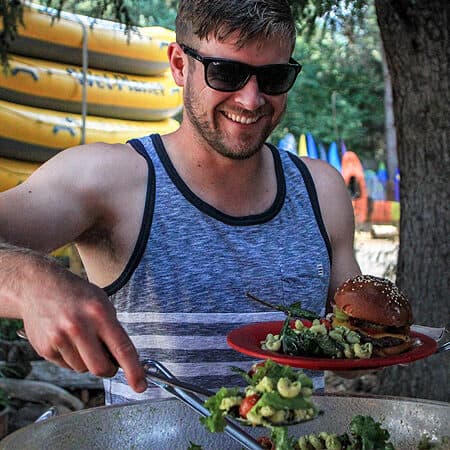 A rafter serves himself salad at a catered rafting event BBQ.