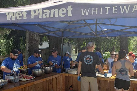 Rafters add condiments to their burgers while two Wet Planet employees serve more guests at a BBQ.