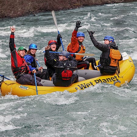 A group of paddlers in a paddle raft celebrate and wave to the camera while rafting on the raft guide school.