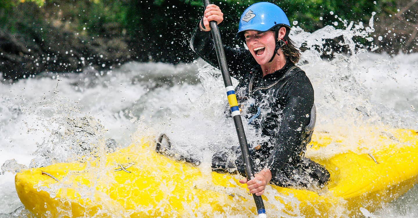 A kayaking student smiles while running a rapid on a beginner river kayaking course.