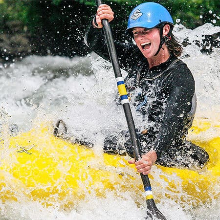 A kayaking student smiles while running a rapid on a beginner river kayaking course.