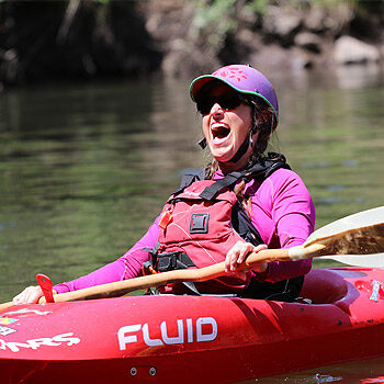 A female kayaker on a beginner kayak instruction course yells in celebration while floating in her kayak - wet planet whitewater Washington, Oregon, and Idaho