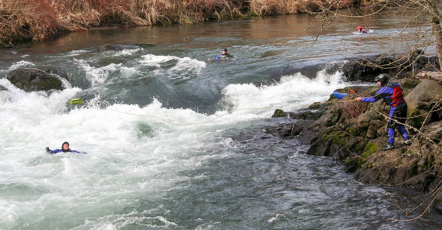 A student on a river rescue course throws a rope to a swimmer in the middle of the river.