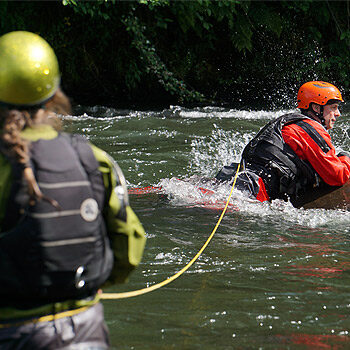 During a river rescue coruse, a student swims out to a rock while being belayed on a rope.