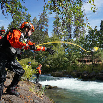 A student on a Rescue 3 International Swiftwater Rescue Technician course throws a rescue rope to a swimmer in the river.