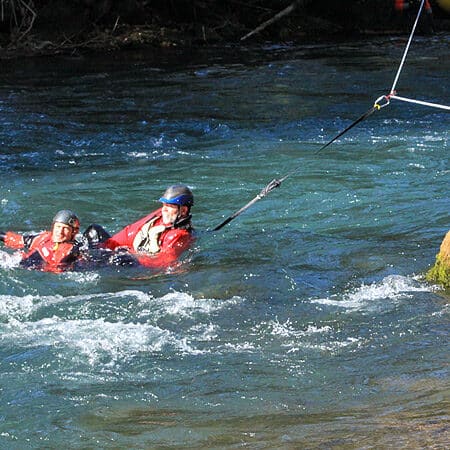 A student holds onto a victim in the river while using a tension diagonal system to cross the river on river rescue course.