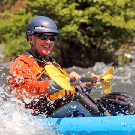 A man smiles while paddling a sit on top kayak in a rapid.