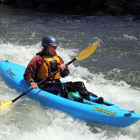 A woman paddles a sit on top kayak in a rapid and smiles.