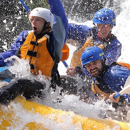 A group of rafters yells in excitement and their raft guide smiles while splashing through Rattlesnake Rapid on a White Salmon River rafting trip in Washington.