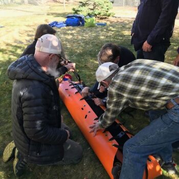 Students on a wilderness first responder course practice packaging a patient into a litter.