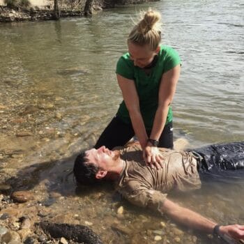 A female students practices performing CPR on a patient who is lying in the water.