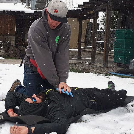 A student on a Wilderness First Responder Course practices performing CPR on a patient lying in the snow.