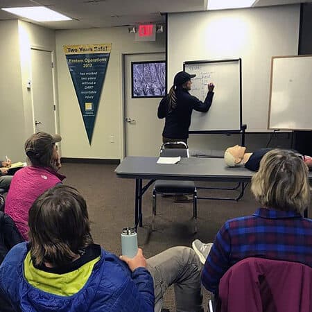 An instructor writes on the dry erase board in front of students during a wilderness first responder course.