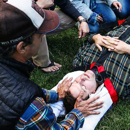 Students on a wilderness first responder course hold a patient's head stable while he is being strapped to a backboard.