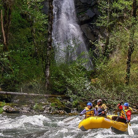 On the Wind River in Washington a group of rafters paddles past a waterfall.