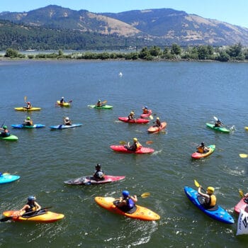 A large group of kayakers float together in flatwater with mountain views in the background on a kids kayak youth program.