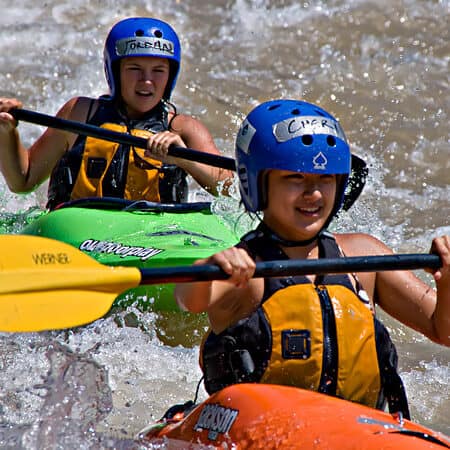 Two teenage female kayakers run a rapid together in their kayaks.